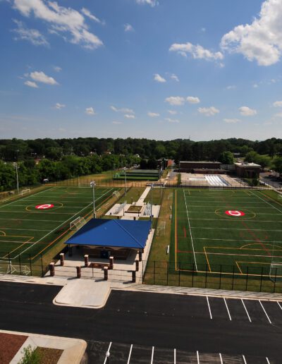 Aerial view of an outdoor sports complex with multiple fields and parking spaces, under a clear sky.