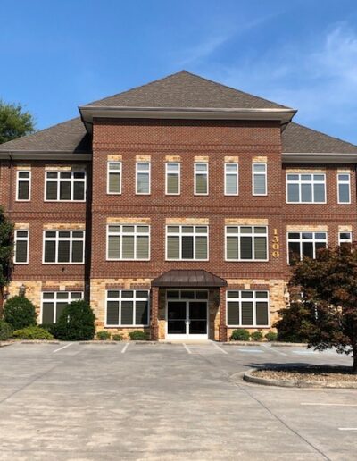 Three-story brick building with central entrance and parking area in front.