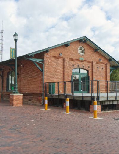 A brick building with a green roof and arched windows serving as a train station platform with clear skies in the background.